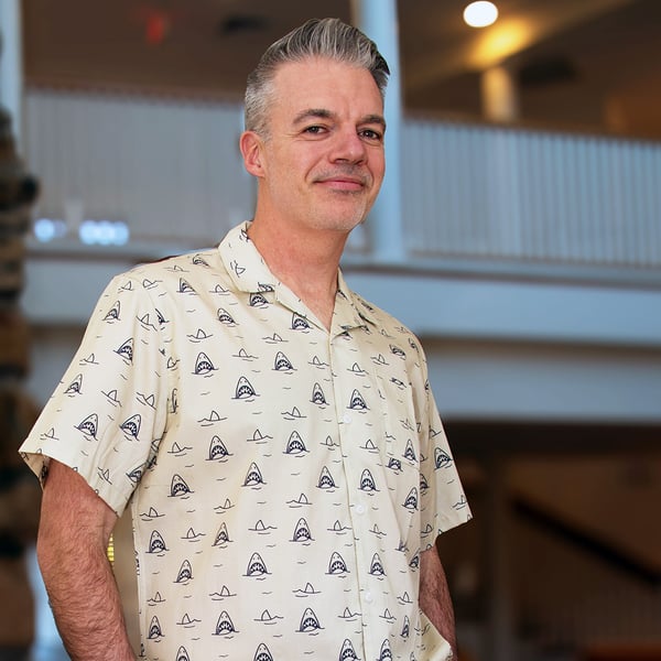 A man with short hair wears WHOI's short sleeve shark button-up.