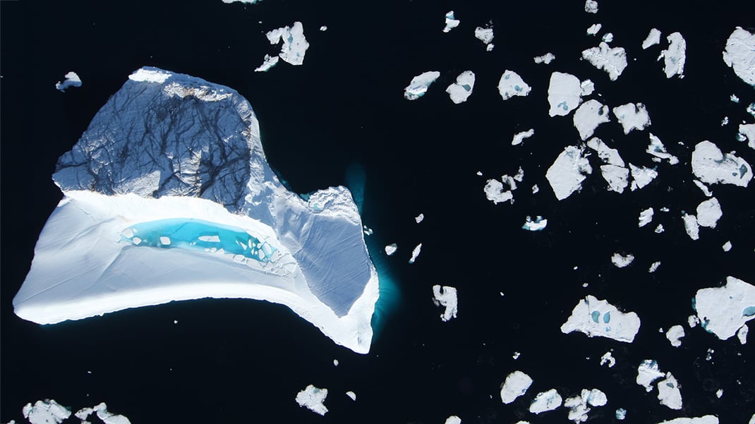(Left) An iceberg sits in dark cold water with chunks of ice scattered to the right.