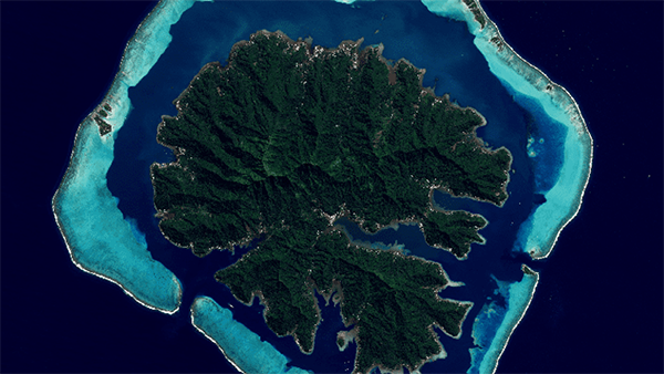A bird's eye view of an island surrounded by a ring of shallow reefs creating a lagoon 