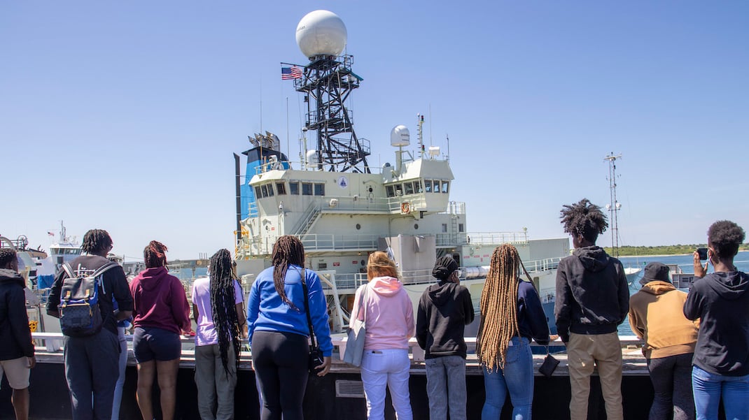 A group of 10 youths look at at WHOI research vessel