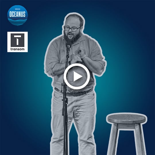 WHOI research engineer Beckett Colson talks into a microphone with a stool on his right side. He's wearing a button-up shirt tucked into a pair of trousers with a belt.