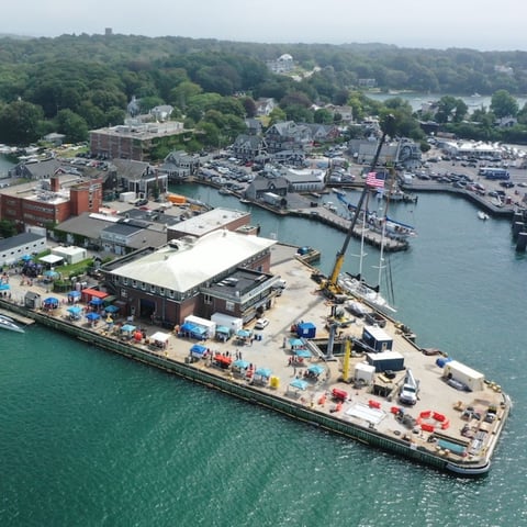 An aerial image showing Iselin Dock in Woods Hole, Massachusetts. Patrons are seen walking around tents lining the dock as a part of the Woods Hole Science Stroll.