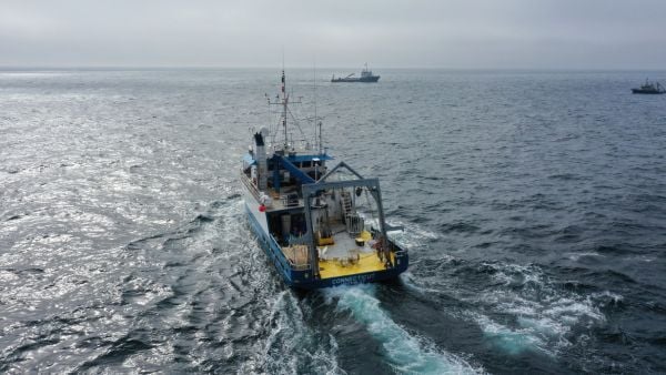 A small research vessel with an a-frame travels toward the horizon making a small wake.