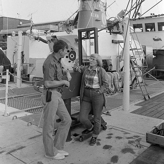 (Left) A man talks to a women named Ruth Turner (right) on the deck of a ship. Behind them is the submersible Alvin.